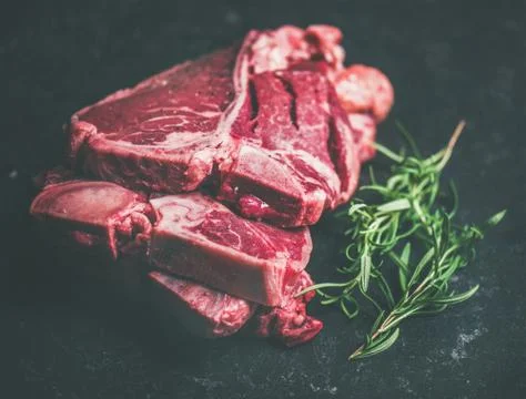 Raw beef meat t-bone steaks with rosemary on black background Stock Photos