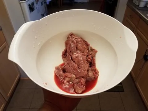 Raw beef with red liquid in white bowl or container in kitchen Stock Photos