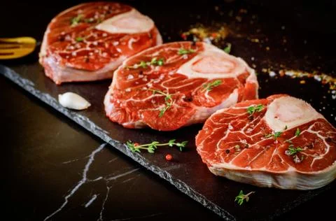 Raw beef shank and spices for preparing ossobuco dish on black background. Stock Photos