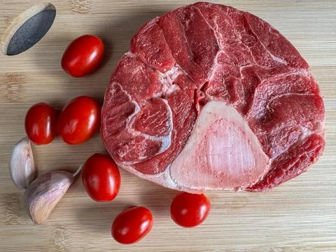 Raw beef shank steak with bone surrounded by cherry tomatoes and garlic clo.. 스톡 사진