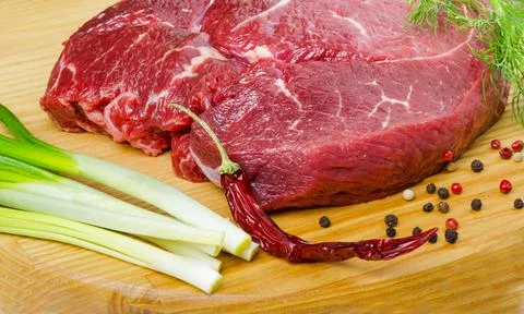 Raw beef steak and chilli pepper on wooden board, close up Stock Photos