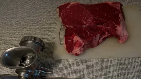Raw beef steak on cutting board next to metal meat grinder against textured.. Video stock 344422094