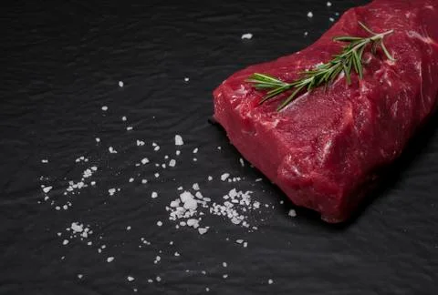Raw beef steak on a cutting board with rosemary and spices. Stock Photos