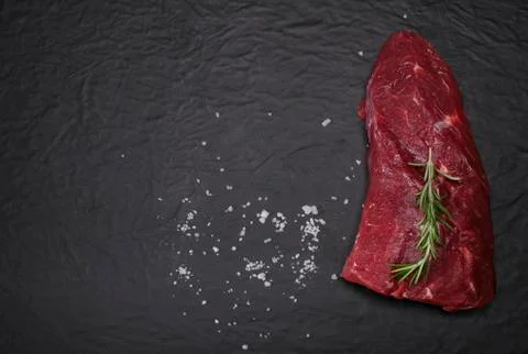 Raw beef steak on a cutting board with rosemary and spices. Stock Photos