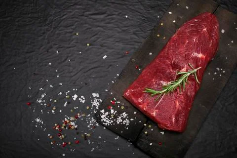 Raw beef steak on a cutting board with rosemary and spices. Stock Photos