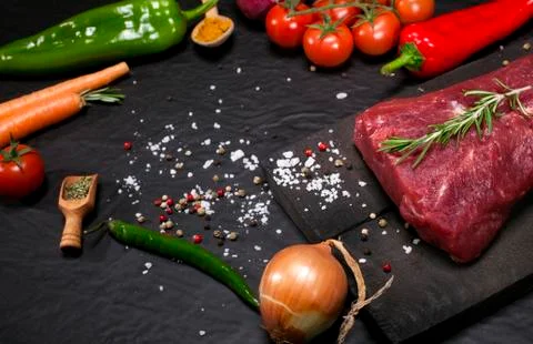 Raw beef steak on a cutting board with rosemary and spices. Stock Photos