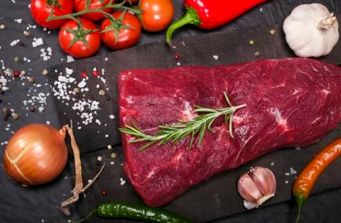 Raw beef steak on a cutting board with rosemary and spices. Stock Photos