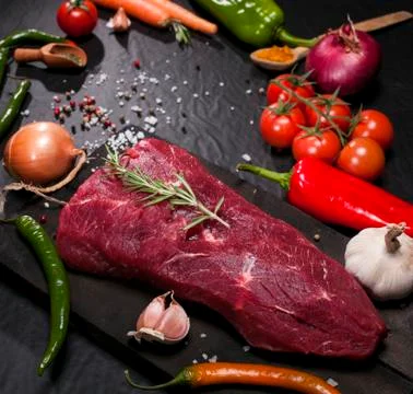 Raw beef steak on a cutting board with rosemary and spices. Stock Photos