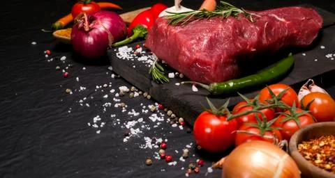 Raw beef steak on a cutting board with rosemary and spices. Stock Photos
