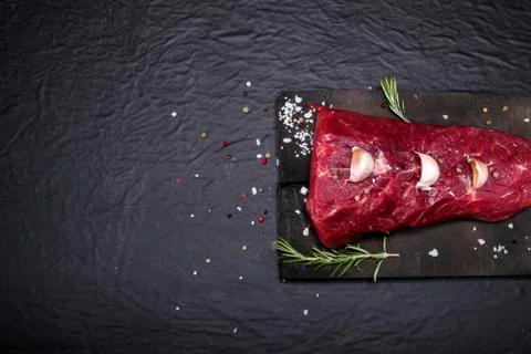 Raw beef steak on a cutting board with rosemary and spices. Stock Photos