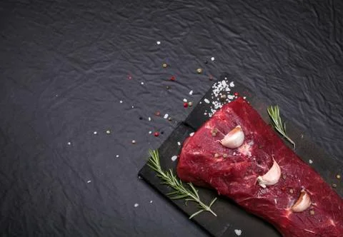 Raw beef steak on a cutting board with rosemary and spices. Stock Photos