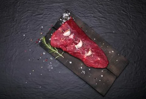 Raw beef steak on a cutting board with rosemary and spices. Stock Photos