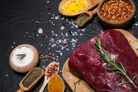 Raw beef steak on a cutting board with rosemary and spices. Stock Photos