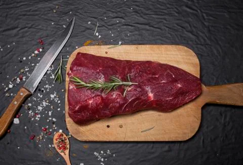 Raw beef steak on a cutting board with rosemary and spices. Stock Photos