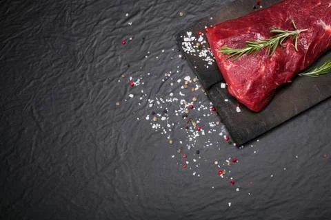 Raw beef steak on a cutting board with rosemary and spices. Stock Photos