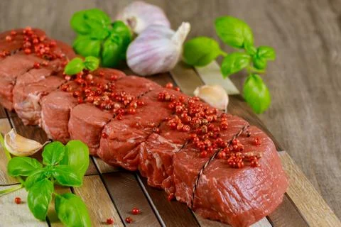 Raw beef steak with garlic and basil on wooden board. Stock Photos