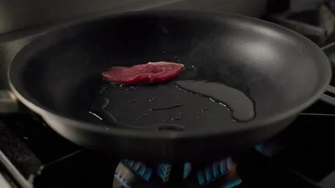 Raw beef steak placed into hot pan with oil on gas stove Stock Footage 313055776