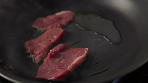 Raw beef steak placed into hot pan with oil on gas stove Stock Footage 313055807
