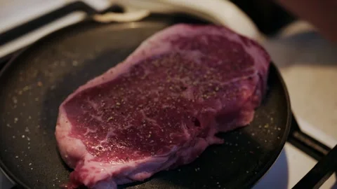 Raw beef steak seasoned with pepper and salt before cooking on frying pan. Stock Footage 339661248