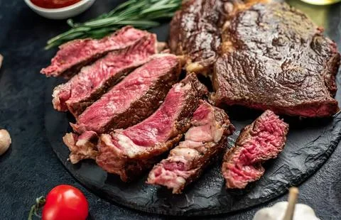Raw beef steak sliced on black stone with cherry tomato Stock Photos