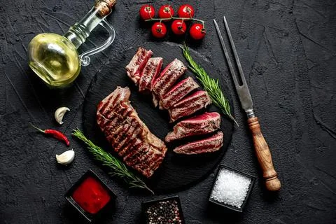 Raw beef steak slices on a black cutting board with spices Stock Photos