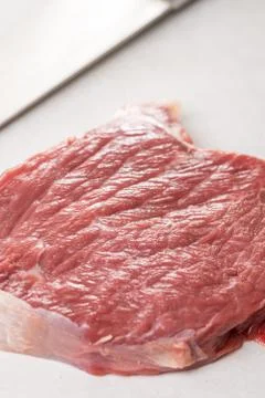 Raw beef steak on the white marble table with chef knife in the background Stock Photos