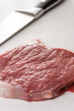 Raw beef steak on the white marble table with chef knife in the background Stock Photos
