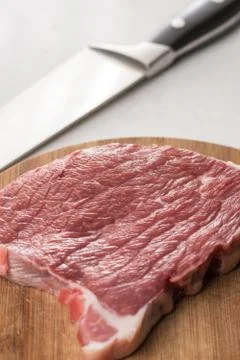 Raw beef steak on the white marble table with chef knife in the background Stock Photos