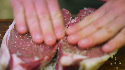 Raw beef steaks being seasoned with salt and pepper on a wooden cutting board Stock Footage 336656785