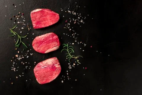 Raw beef steaks with salt, pepper and rosemary on a black background Fotos Stock
