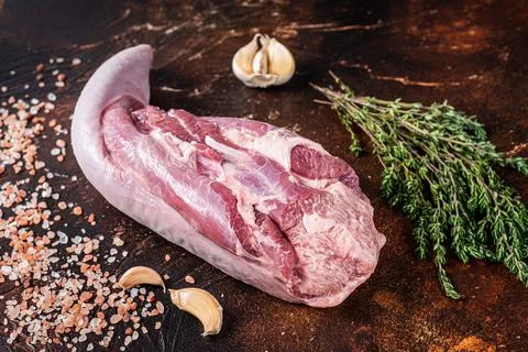 Raw beef tongue on kitchen table with herbs. Dark background. Top view Stock Photos