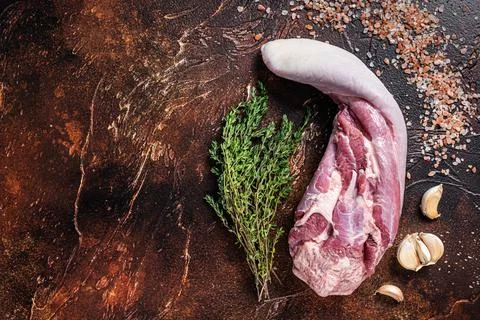 Raw beef tongue on kitchen table with herbs. Dark background. Top view. Copy Stock Photos