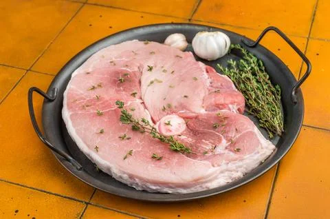 Raw bone in pork shoulder in round pan with thyme and garlic on yellow tile.. Stockfoto's