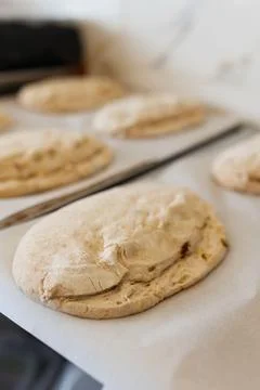 Raw bread loaves on baking trays with parchment, artisan bakery preparation Stockfoto's