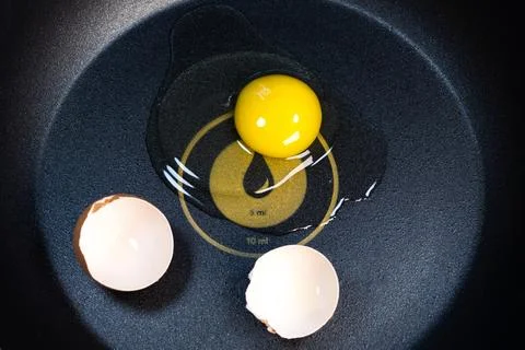 Raw broken egg and egg shells in a pan with a dispenser. Fried egg on the pan Stock Photos