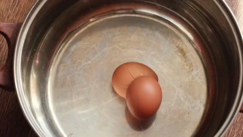 A raw brown chicken egg falls into a metal cooking pot from above and break.. Stock Footage 344112400