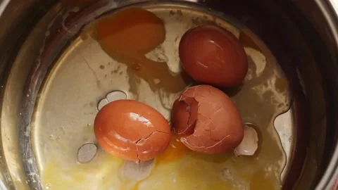 A raw brown chicken egg falls into a metal pot from above alongside several.. Stock Footage 344112425