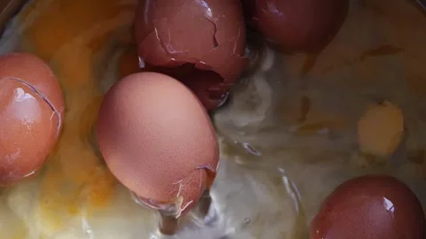 A raw brown chicken egg falls into a metal pot in a close-up overhead shot .. Stock Footage 344112505