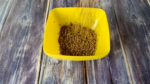 Raw buckwheat is poured from above into a yellow plastic bowl Stock Footage 231594091