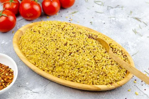 Raw bulgur in a bamboo plate on grey table with tomatoes and seasoning Stock Photos