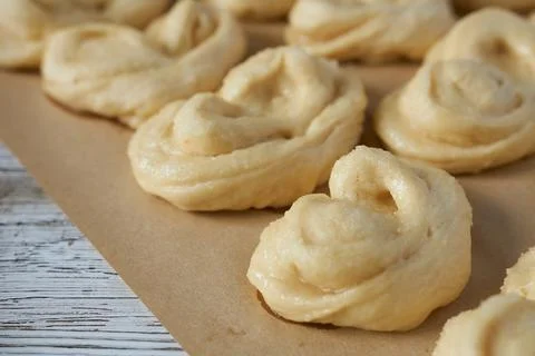 Raw buns on a baking sheet on a white wooden background. Yeast dough. Stock Photos