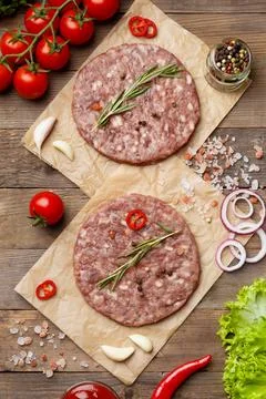 Raw burger patties on parchment and hamburger ingredients on wooden backgro.. Stock Photos
