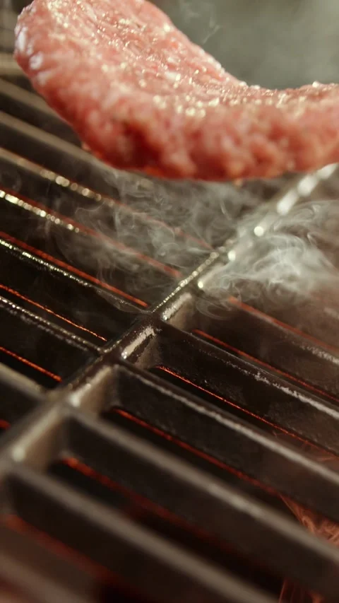 Raw burger patty placed on hot grill grate with seasonings falling on meat .. Stock Footage 337441113