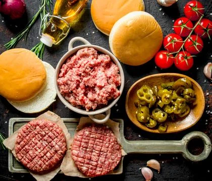 Raw burgers with ground beef, oil, buns and tomatoes. Stock Photos