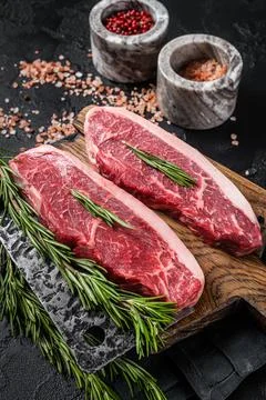 Raw cap rump beef meat steak or top sirloin on butcher board. Black background Stock Photos
