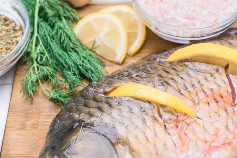 Raw carp fish stuffed with lemon slices lies on a cutting board, close-up Stock Photos