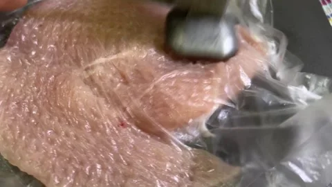 Raw chicken breast covered with plastic wrap being pounded flat with a meat.. Stock Footage 314729511