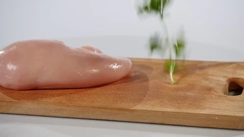 Raw chicken fillet and parsley falls on a wooden board Stock Footage