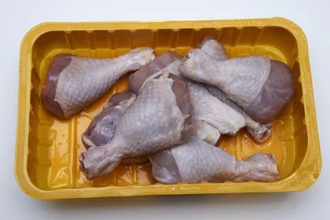 Raw chicken legs in a plastic container on a white Stock Photos