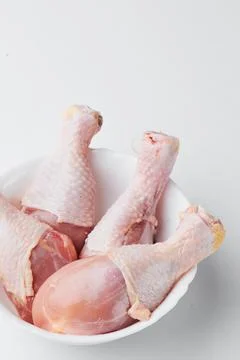 Raw chicken legs on a white plate isolated on a white background. Close-up Stock Photos